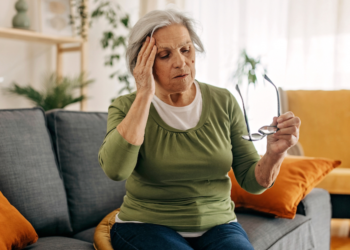 An older woman sitting on her couch holding her head