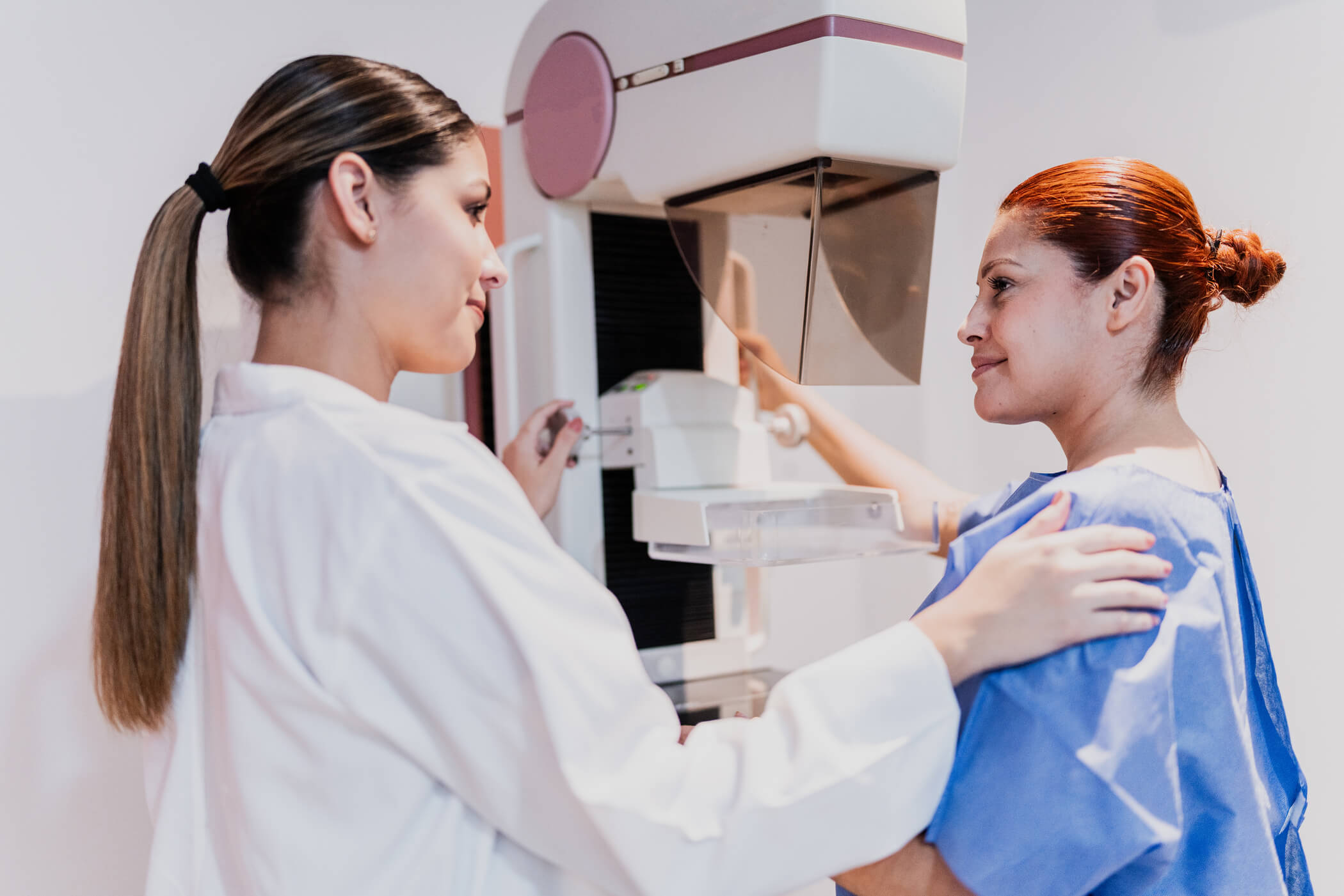 Imaging specialist performing a mammogram on a smiling woman.