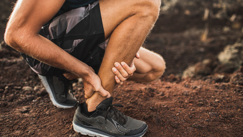 man crouching down holding his Achilles heel 